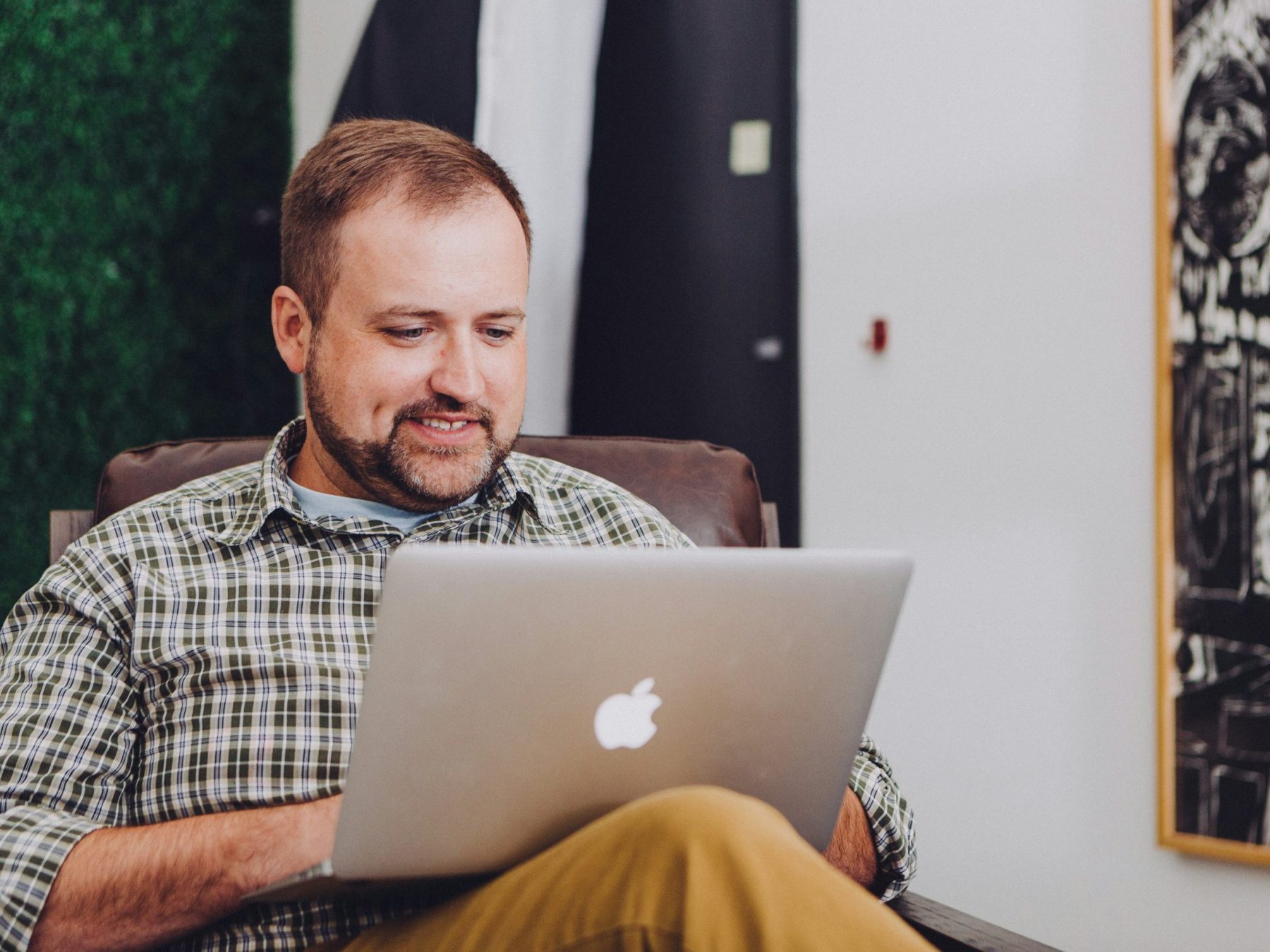 A smiling man with a laptop resting on his knees.